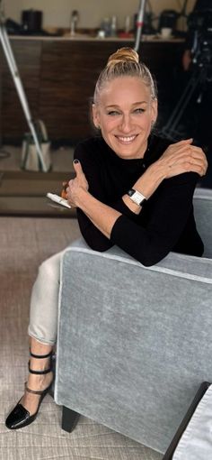 a woman sitting on top of a gray couch next to a white chair with her arms crossed