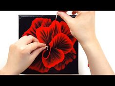 someone is painting a red flower on a black square piece of art with acrylic paint