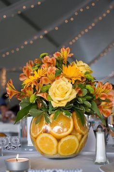 a vase filled with oranges and yellow flowers sitting on top of a table next to candles