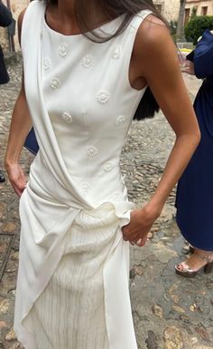 a woman in a white dress standing on a cobblestone street with her hands on her hips