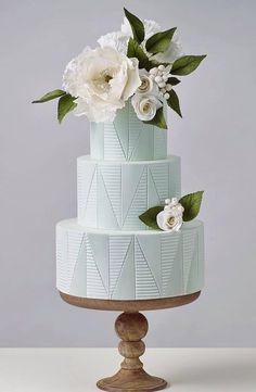 a three - tiered cake with white flowers on top and green leaves around the edges