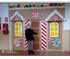 a woman standing in front of a cardboard gingerbread house decorated with candy canes