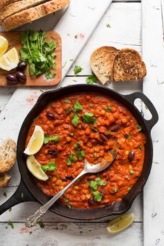 a skillet filled with beans and bread on top of a white table next to sliced lemons