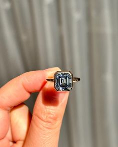 a person holding up a ring with an emerald colored stone in it's middle