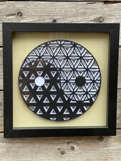 a black and white circular artwork hanging in a frame on a wooden wall next to wood planks