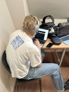 a man sitting at a desk with two laptops and headphones in front of him