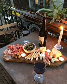 a table with wine, cheese and meats on it in front of a candle