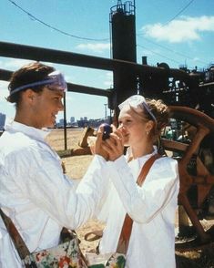 a man and woman standing next to each other in front of an old machinery wheel