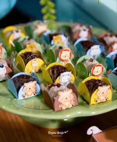 there are many small cupcakes with animals on them sitting on a green plate