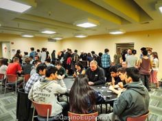 a group of people sitting at tables in a room with many other people standing around