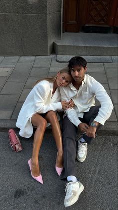 a man and woman sitting on the ground next to each other with their arms around each other