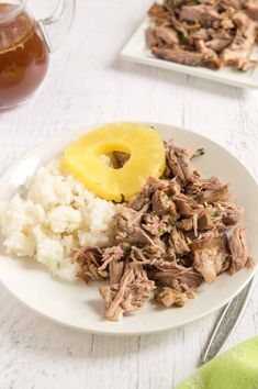 a white plate topped with meat, rice and a pineapple next to a glass of tea