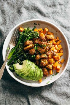 a white bowl filled with vegetables and meat on top of a gray cloth next to a fork