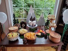 a table topped with lots of food next to a window filled with trees and balloons