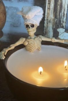 a skeleton sitting in a bowl with candles