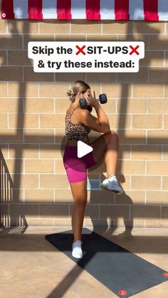 a woman in pink shorts and white sneakers is doing exercises on a black mat with a red striped wall behind her