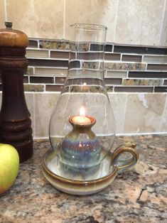 a glass teapot with a candle inside sits on a counter next to an apple