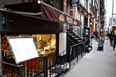 the sidewalk is lined with shops and people are walking down the street in front of them