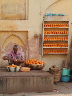 a man sitting on the ground in front of some baskets filled with oranges and other fruit