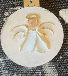 a white ornament with a gold angel on it's side and two small wooden spoons next to it