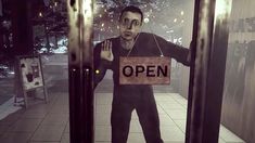 a man is holding an open sign in front of his face while standing outside the door