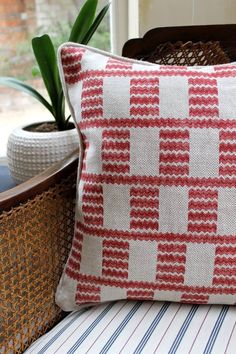 a red and white pillow sitting on top of a chair next to a potted plant