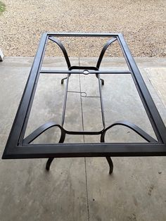 a black metal table sitting on top of a cement floor next to a gravel field