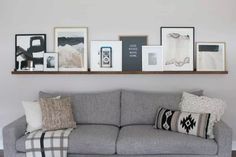 a gray couch sitting under a wooden shelf filled with pictures and framed art on it