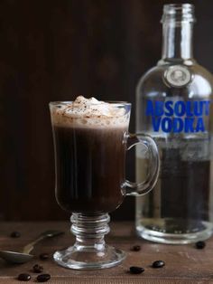 a glass cup filled with hot chocolate and whipped cream next to a bottle of vodka