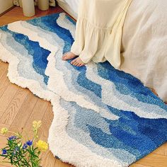 a woman laying on the floor in front of a bed with blue and white rugs