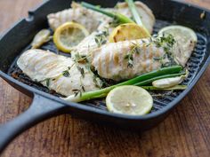 fish with lemon slices and green beans in a skillet on a wooden table top