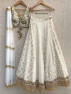 This white and gold blouse is embellished with hand embroidered mirror work, cutdanna and swarovski stone.   The blouse is paired with a multi kali butti lehenga with borders at the hem.  The outfit is completed with a layered tassel dupatta. Lehenga With Mirror Work, Kali Lehenga, Katori Blouse, Mirror Work Lehenga, Mirror Work Blouse, Indian Outfits Lehenga, Lehenga Designs Simple, Instagram Luxury, Salwar Kamiz