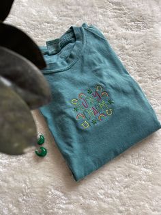 Get ready for St. Patrick's Day with this Lucky Charms-inspired design on a dark aqua Comfort Colors T-Shirt! This shirt is also perfect for any Lucky Charms connoisseur.  -Sweatshirt brand: Comfort Colors -Sizes available: Adult Small - Adult 3XL -Fit: comfortable & slightly oversized - I'd recommend your normal size or size up for a true oversize fit -Machine embroidered with love! Green Crew Neck T-shirt With Custom Embroidery, Trendy Cotton T-shirt With Custom Embroidery, Green Cotton Top With Embroidered Graphics, Casual T-shirt With Multicolor Embroidery And Logo, Trendy Crew Neck T-shirt With Letter Embroidery, Green Crew Neck Top With Embroidered Text, Green Embroidered Text Crew Neck Top, Green Cotton Tops With Embroidered Logo, Green Cotton Top With Embroidered Logo