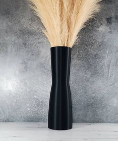 a tall black vase with some brown and yellow feathers in it's center, against a gray background