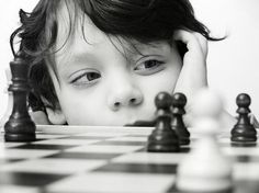 a young boy is playing chess with his hands on the head and looking at the camera