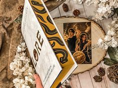 an open book on a wooden table with white flowers and pineconis around it