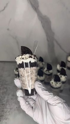 a person in white gloves holding up a cupcake with black and white frosting