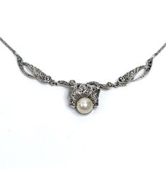 This iconic Art Deco necklace dates aprox from the 1930s. It is solid silver decorated with marcasite gemstones and a faux pearl. Marking: no markings tests as solid silver Size: Just over 15 inches long (38.5 cm). The centre part measures 7.5 cm long Weight: 6.5 grams Condition: Very good condition, no missing stones. Stunning dress piece, find more unique ladies chokers in my shop. https://www.etsy.com/uk/shop/perdisjewellerybox?search_query=marcasite+necklace Antique Pearl Pendant Necklace For Formal Occasions, Antique White Gold Necklace With Pearl Pendant, Antique Pearl Necklace For Formal Occasions, Elegant Silver Pearl Necklace With Intricate Design, Ornate Round Necklaces With Pearl Pendant, Ornate Silver Necklace With Pearl Pendant, Ornate Round Necklace With Pearl Pendant, Ornate Formal Necklace With Oxidized Finish, Vintage White Gold Jewelry With Pearl Pendant