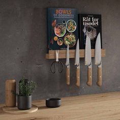 three knives are hanging on the wall next to two cookbooks and a potted plant