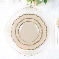 a white and gold place setting with flowers on the table in the backgroud