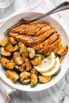 a white bowl filled with grilled zucchini and lemon wedges next to a fork