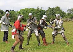 four men dressed in medieval armor are playing with each other on the green grass field