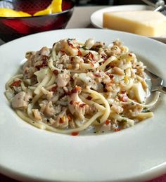 a white plate topped with pasta covered in meat and sauce next to a bowl of cheese