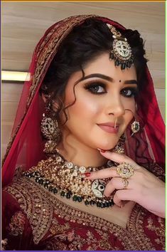 a woman in a red and gold bridal outfit with jewelry on her head, posing for the camera