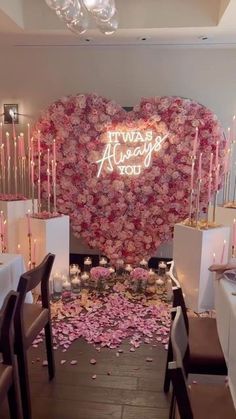 a room filled with lots of tables covered in pink flowers and candles next to a heart shaped wall