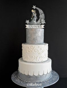 a three tiered white cake with silver frosting and an image of a woman on top