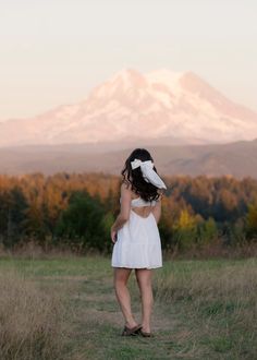 a woman in a white dress standing on a field with mountains in the back ground