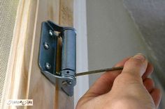 a person holding a pair of scissors in their hand near a door with a hinge