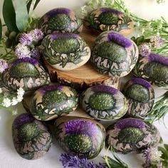 purple and green painted rocks sitting on top of a wooden stump next to some flowers