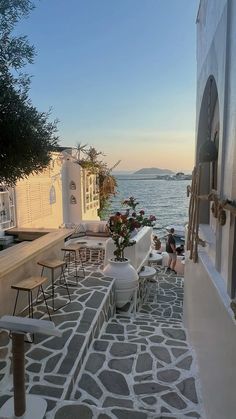 an outdoor seating area next to the ocean with flowers in vases on tables and chairs